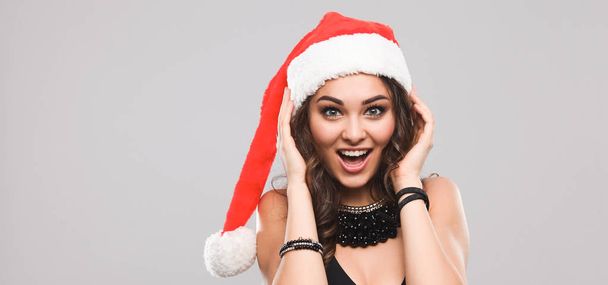 Attractive smiling woman in Santa Cap. Isolated over a gray background. - Foto, afbeelding