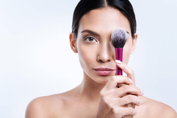 Pleasant dark-haired woman covering her eye with makeup brush - Foto, Imagem