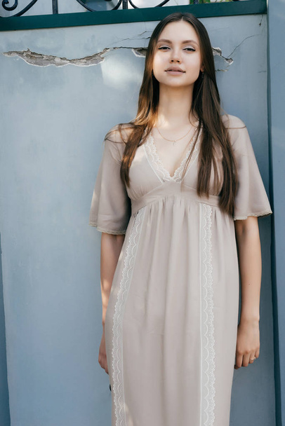 beautiful charming girl in beige dress posing against wall, smiling - Фото, зображення