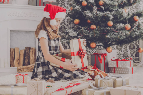 Beautiful girl in santa hat unwrapping christmas presents - Photo, Image