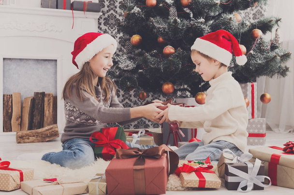 Szczęśliwe dzieci w santa kapelusze rozpakowaniu świątecznych prezentów - Zdjęcie, obraz