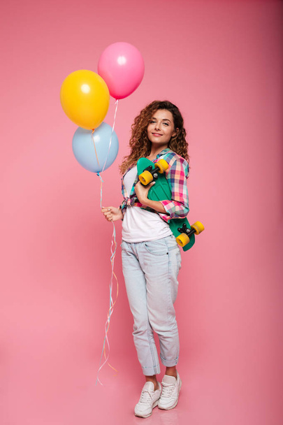 Young woman with air balloons and skateboard looking camera isolated - Foto, afbeelding