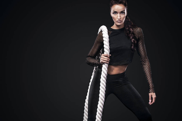 Sporty beautiful woman with battle rope makes fitness exercising at black background to stay fit - Foto, immagini