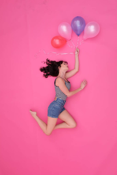 A black-haired girl, flying on inflatable balls on a pink background. - Zdjęcie, obraz