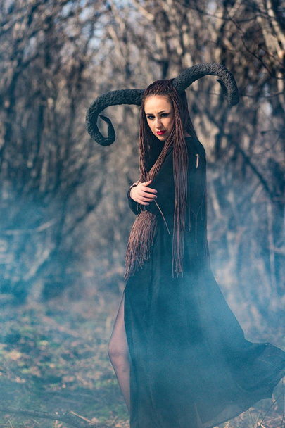 schöne Frau als Hexe im Regenmantel und mit Hörnern zu Halloween verkleidet - Foto, Bild