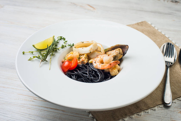 Italian black spaghetti with cuttlefish ink, mussels, tomatoes and green basil on the table. - 写真・画像