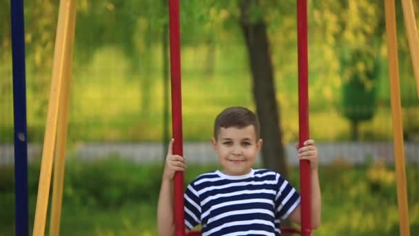 Un niño pequeño con una camiseta a rayas está jugando en el patio de recreo, Swing on a swing.Spring
. - Imágenes, Vídeo