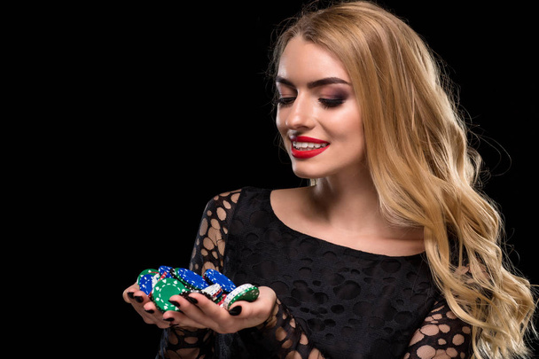 Elegant blonde in a black dress, casino player holding a handful of chips on black background - Foto, Imagem
