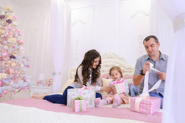 Família amigável no humor festivo para trocar presentes sentados na cama
 - Foto, Imagem