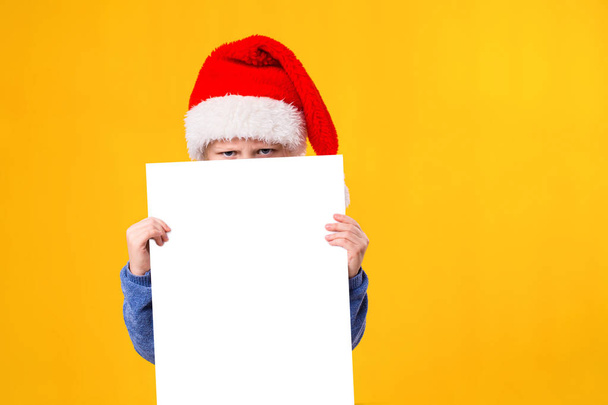 Cute little girl in Santa Claus hat with a white blank paper sheet. Christmas, x-mas, New Year, Winter, people, advertisement, sale concept. - Φωτογραφία, εικόνα