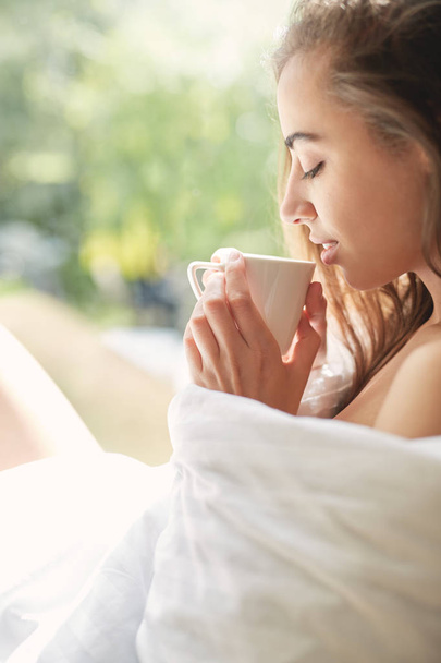 a woman sits on a windowsill with a cup of coffee - Zdjęcie, obraz