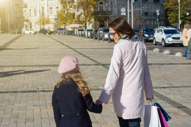 Woman and her little daughter with shopping bags walking along the street - Foto, imagen
