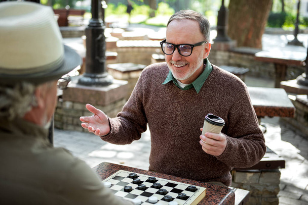 Cheerful mature male pensioners entertaining with draughts in park - Zdjęcie, obraz