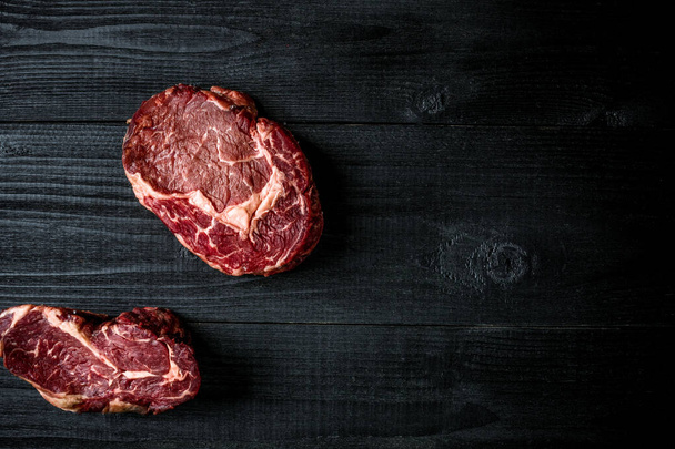 frisches rohes Rindfleisch auf schwarzem Holzgrund. Ansicht von oben - Foto, Bild