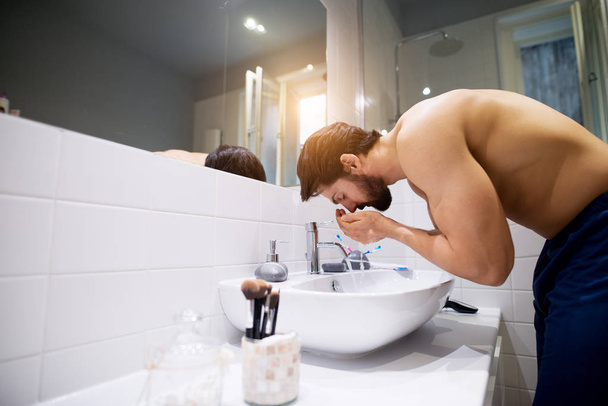 strong muscular shirtless man washing face in bathroom - Foto, imagen