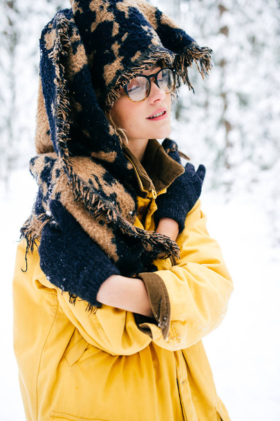 Odd strange young bizarre fancy lonely girl making weird poses in winter snowy forest on weekend. Fashionable mad kinky woman in glasses and warm trendy clothes relaxing outdoor. Crazy headdress. - Foto, Imagem