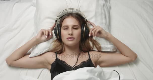 Smyslná žena v posteli s velkými sluchátky - Záběry, video