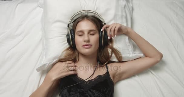 Αισθησιακή γυναίκα στο κρεβάτι με μεγάλα ακουστικά - Πλάνα, βίντεο