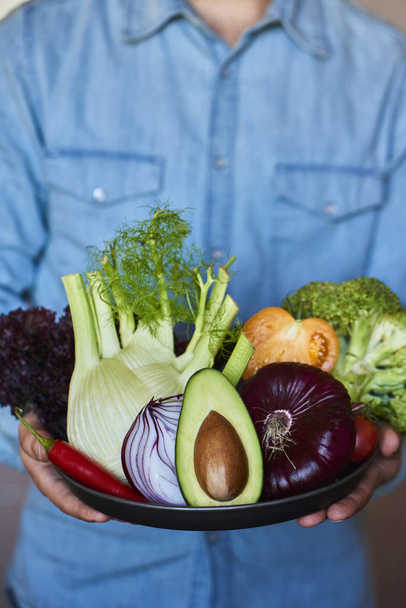 Mains tenant une grande assiette avec différents légumes frais de la ferme. Au
 - Photo, image