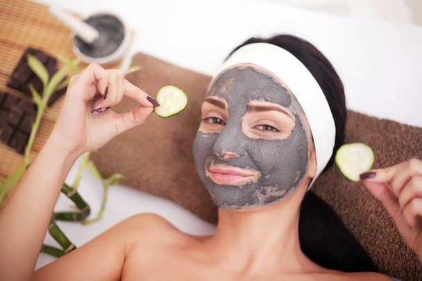 Woman in a beauty salon, wellness. Cosmetic procedure woman's face in the mask mitigating and cucumber slices on eyes - Photo, Image