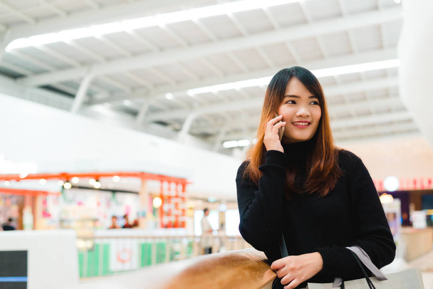 Muotokuva kaunis nuori aasialainen nainen ostoskeskuksessa, hymyillen älypuhelimella verkostoitua sisätiloissa. Turisti nainen käyttää teknologiaa, matkustaa elämäntapa. Ostoskeskus ulkoa vaatekauppa
. - Valokuva, kuva