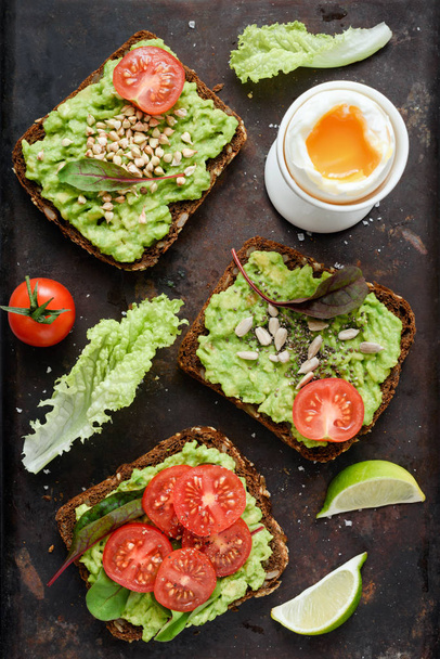 Healthy green veggie toast with avocado, tomato, sprouts and seeds and boiled egg on rusty background - Photo, image