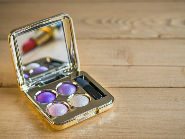 Eye shadow and reflected in the mirror lipstick on a vintage wooden table. - Photo, Image