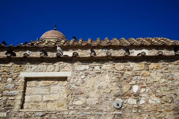 Szene der alten klassischen kleinen Kirche in erdfarbenem Naturstein mit Tauben auf Terrakotta-Dachziegel mit klarem blauem Himmelshintergrund - Foto, Bild