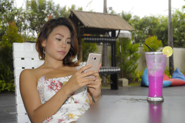 счастливая азиатка расслабился на открытом воздухе в кафе курортной террасе с фруктовым соком с помощью мобильного телефона смс и сетей
 - Фото, изображение