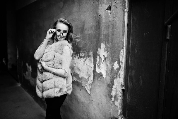 Blonde girl at fur coat and glasses posed against old orange wal - Fotografie, Obrázek
