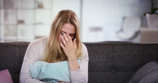 Sad young woman sitting on the couch holding a pillow in front of her - Filmati, video