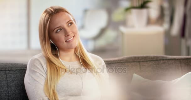 Attractive young lady in modern loft sitting on couch wearing earphones - Metraje, vídeo