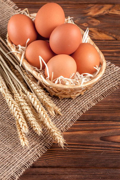 Chicken eggs horizontal banner. Eco farming concept. Red eggs and wheat ears on piece of sacking on brown wooden textured background. Organic food. - Photo, Image