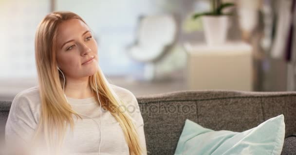 Beautiful young woman listening to music on the couch at home - Filmmaterial, Video