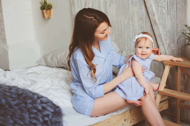 glückliche Mutter und 9 Monate altes Baby im passenden Pyjama, die morgens im Schlafzimmer spielen. Gemütliches Familienwochenende. - Foto, Bild