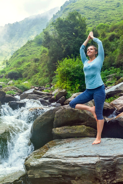 Frau in Yoga-Asana Vrikshasana-Baum posiert am Wasserfall im Freien - Foto, Bild
