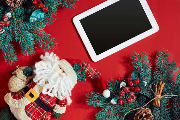 Decoraciones navideñas y tableta blanca con pantalla negra sobre fondo rojo caliente. Tema Navidad y Año Nuevo. Lugar para su texto, deseos, logotipo. Prepárate.
. - Foto, imagen