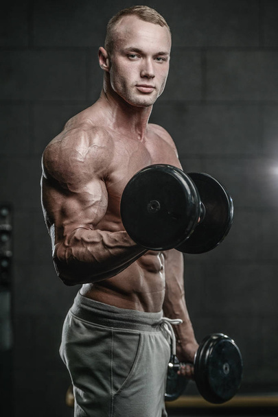Handsome model young man training arms in gym - Foto, Bild