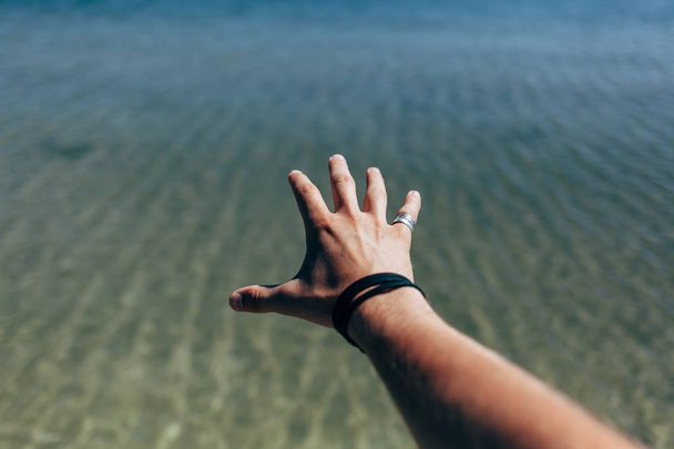 Male hand on a background of the sea - 写真・画像