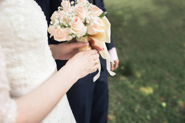 Большой красивый свадебный букет в женских руках. Жених и невеста обнимаются на свадьбе
. - Фото, изображение