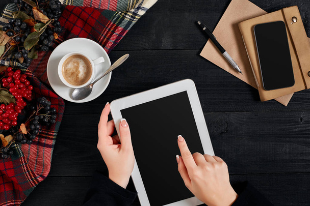 Frauenhände halten das Tablet mit schwarzem Bildschirm über dem Tisch mit einer Tasse Kaffee und Smart - Foto, Bild