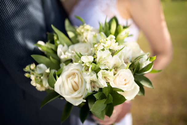 Большой красивый свадебный букет в женских руках. Жених и невеста обнимаются на свадьбе
. - Фото, изображение