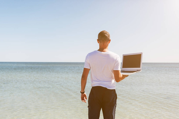 Młody człowiek trzyma laptop biały na tle morza - Zdjęcie, obraz