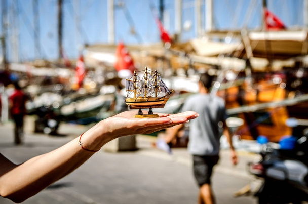 ein kleines Souvenirschiff vor dem Hintergrund großer Schiffe auf dem Bodrum-Damm in der Hand eines Touristen. - Foto, Bild