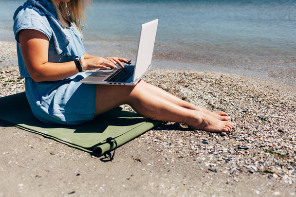 Giovane bella donna seduta con computer portatile sulla spiaggia vicino al mare
 - Foto, immagini