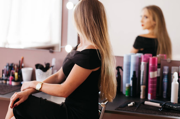 Piękna kobieta w czarnej sukience z profesjonalny makijaż siedzi na krześle w gabinecie kosmetycznym - Zdjęcie, obraz