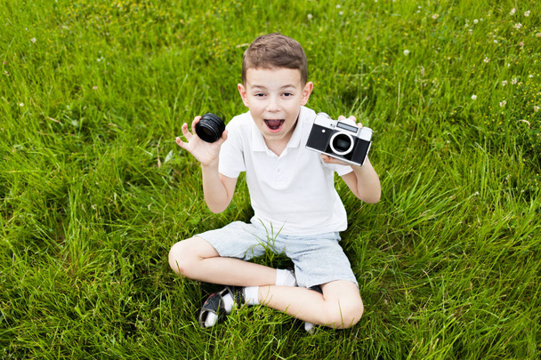 Szczęśliwy chłopiec siedzi na trawie i trzymając aparat retro film - Zdjęcie, obraz