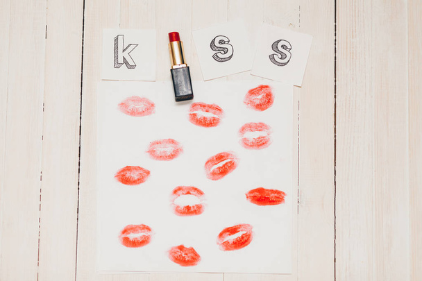 Bovenaanzicht schot van samenstelling met rode lippenstift prints op papier en kus tekst op houten achtergrond - Foto, afbeelding
