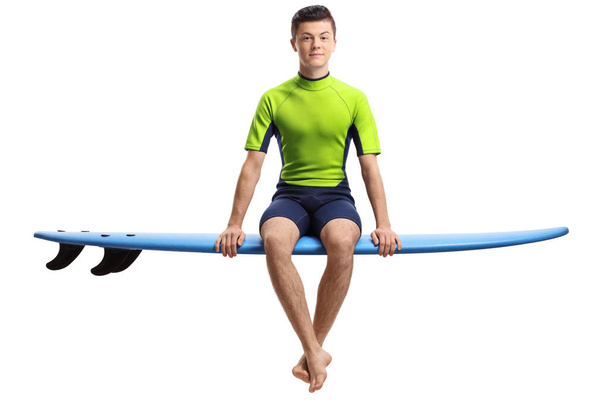 Teenage surfer seated on a surfboard - Фото, изображение