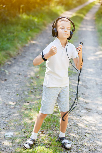 Μικρό αγόρι, φορώντας μεγάλα ακουστικά και ακούγοντας μουσική κάνοντας αστεία πρόσωπα και να χορεύουν - Φωτογραφία, εικόνα
